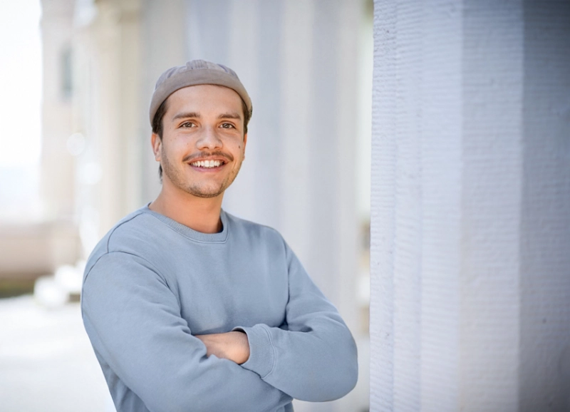 Junger Mann mit hellblauem Pullover und verschränkten Armen